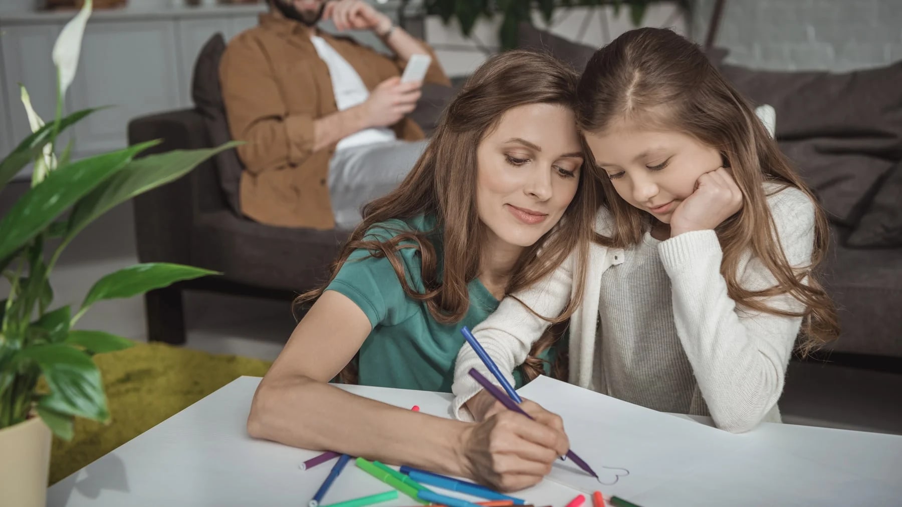 Mulher e menina desenhando juntas com canetinhas coloridas, na mesa da sala