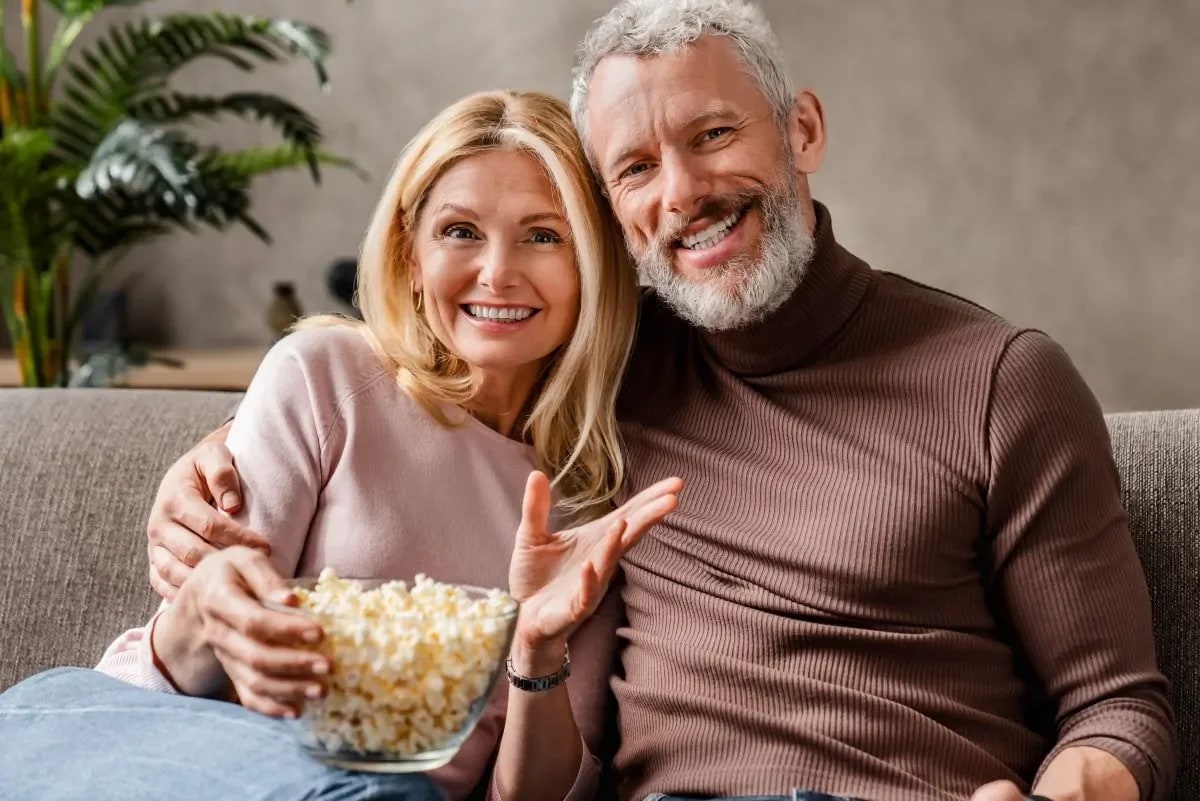 Casal de idosos rindo juntos assistindo filme na sala de estar em momento familiar