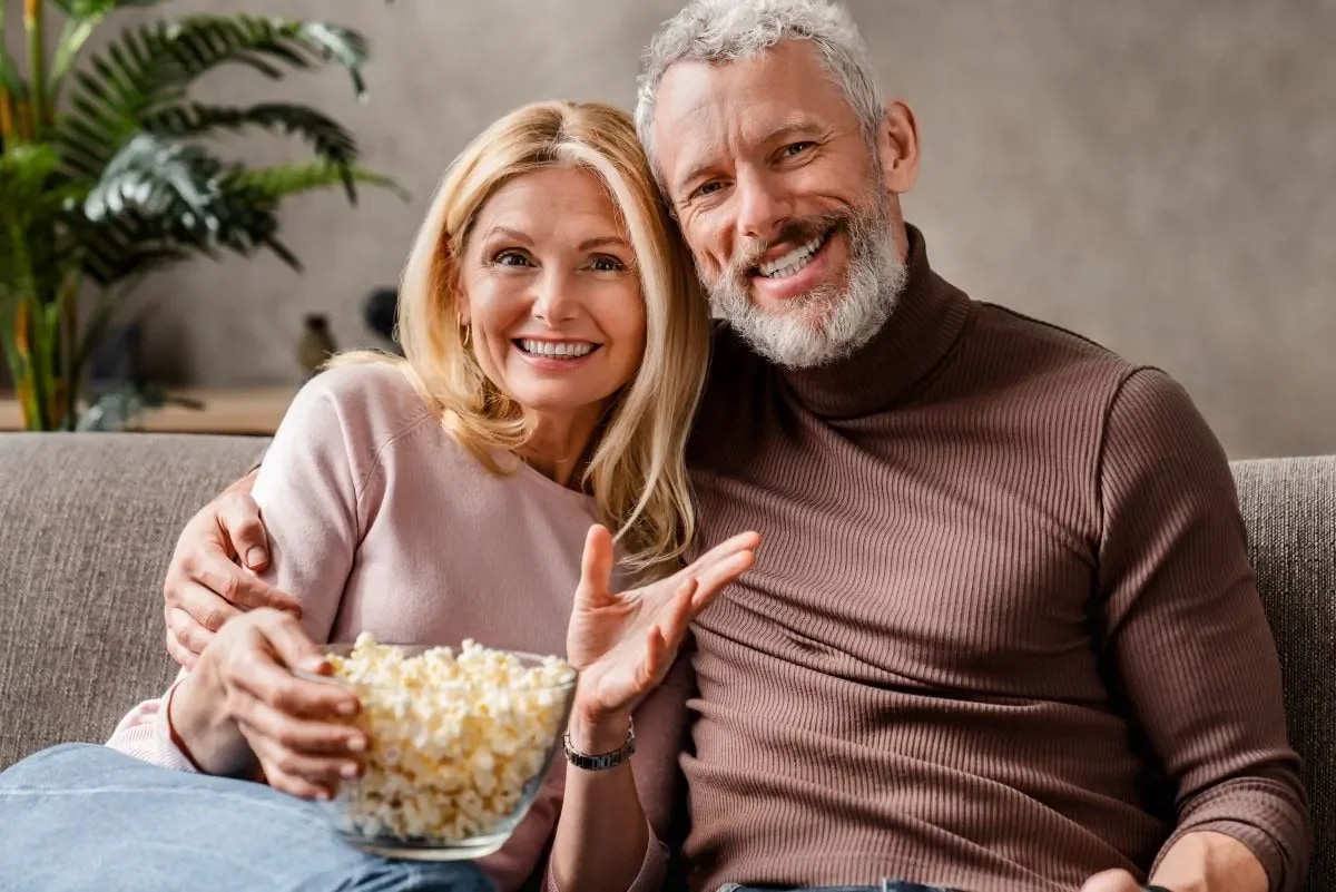 Casal de idosos rindo juntos assistindo filme na sala de estar em momento familiar
