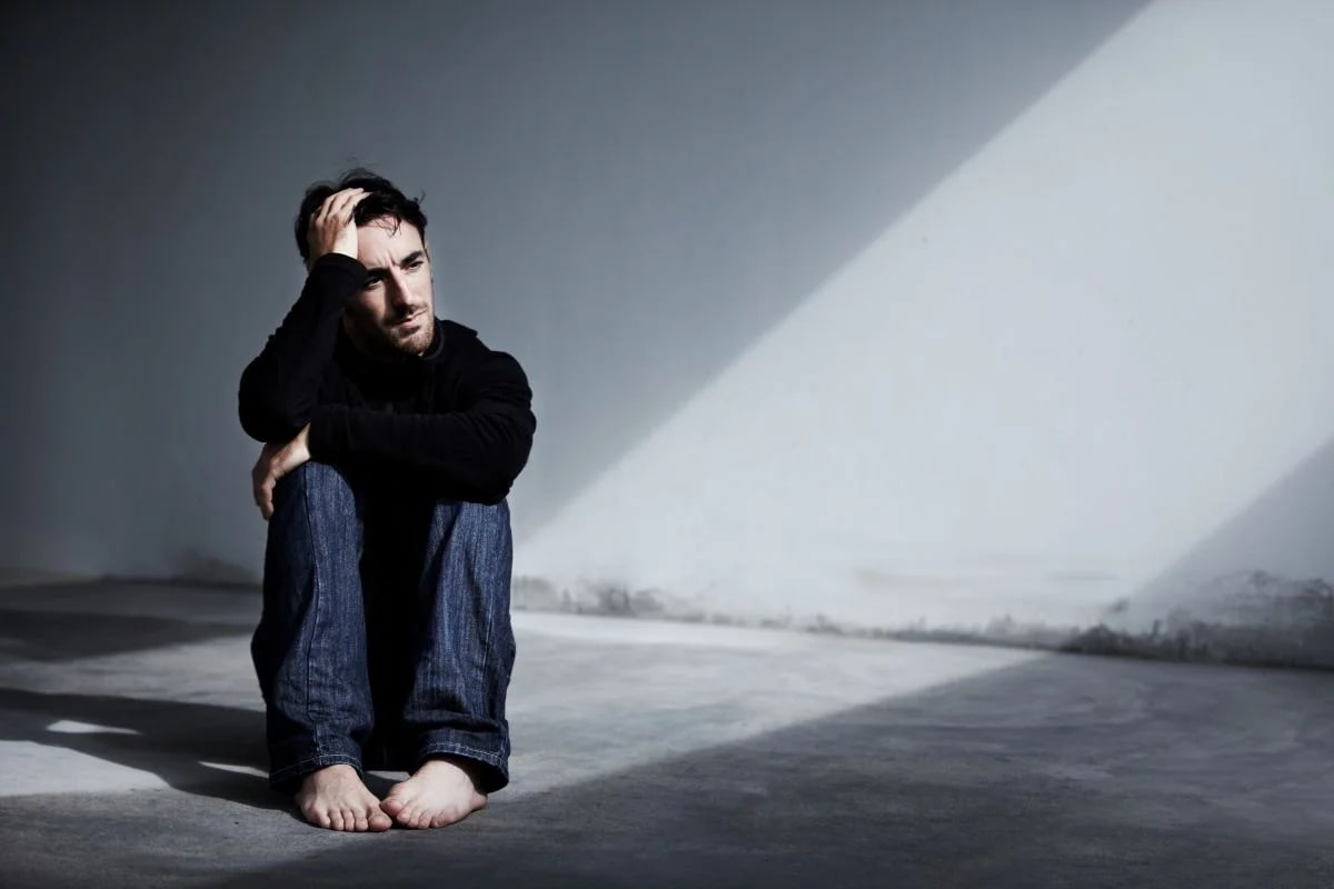 Pessoa em momento de tristeza profunda junto à janela ilustrando sintomas da depressão