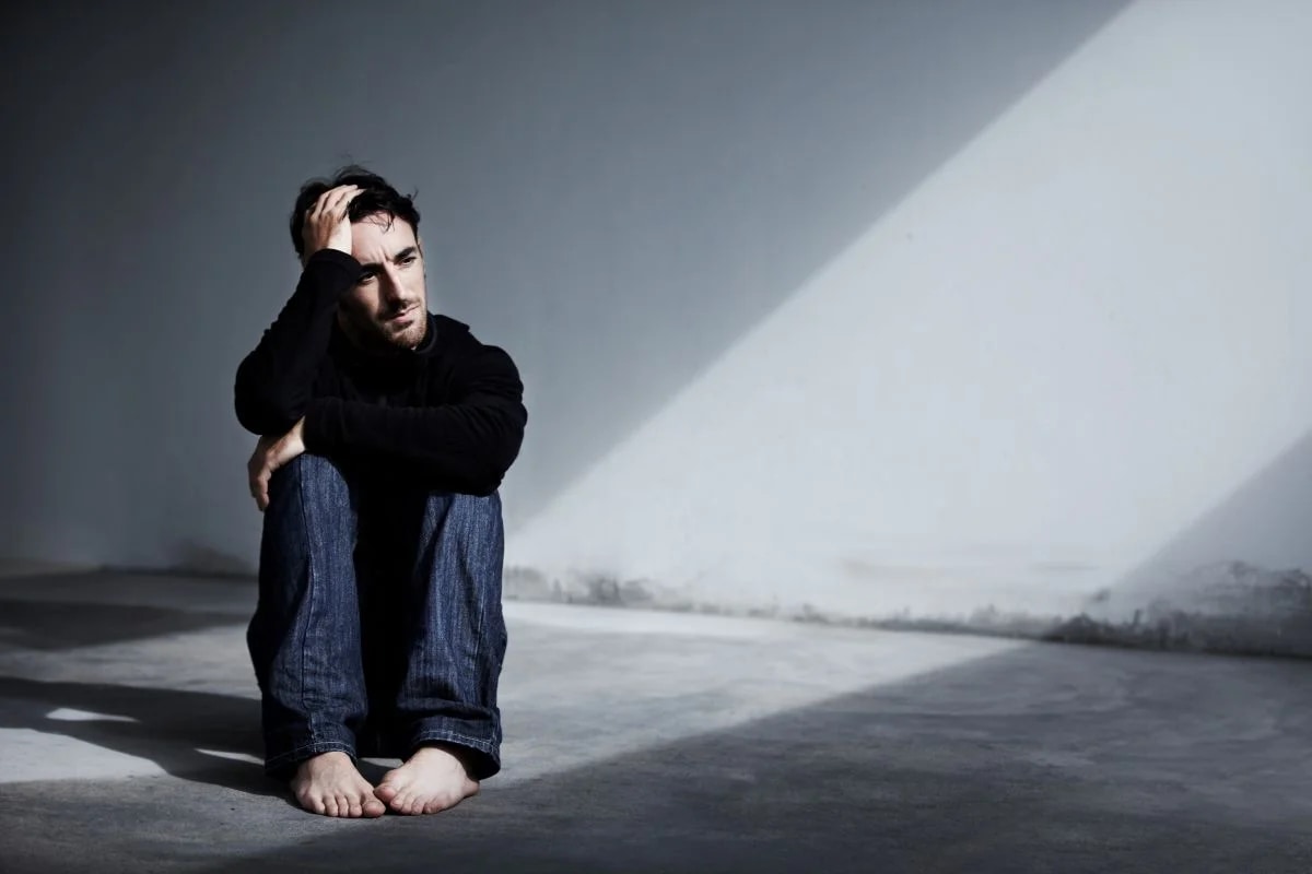 Pessoa em momento de tristeza profunda junto à janela ilustrando sintomas da depressão