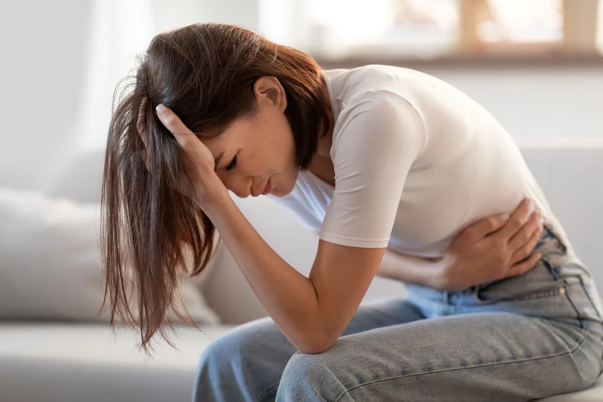 Mulher com cólica menstrual deitada no sofá ilustrando o transtorno disfórico pré-menstrual