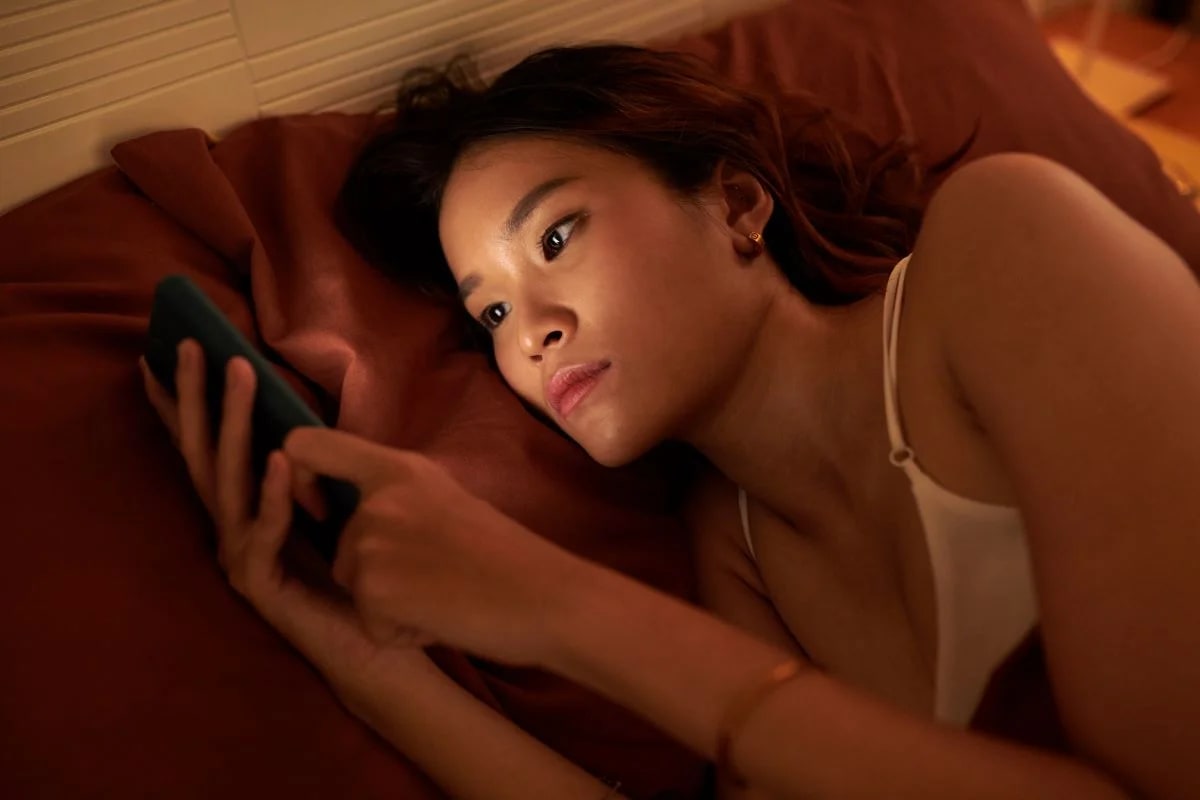 Mulher rolando feed de redes sociais na cama de madrugada, retrato da nomofobia