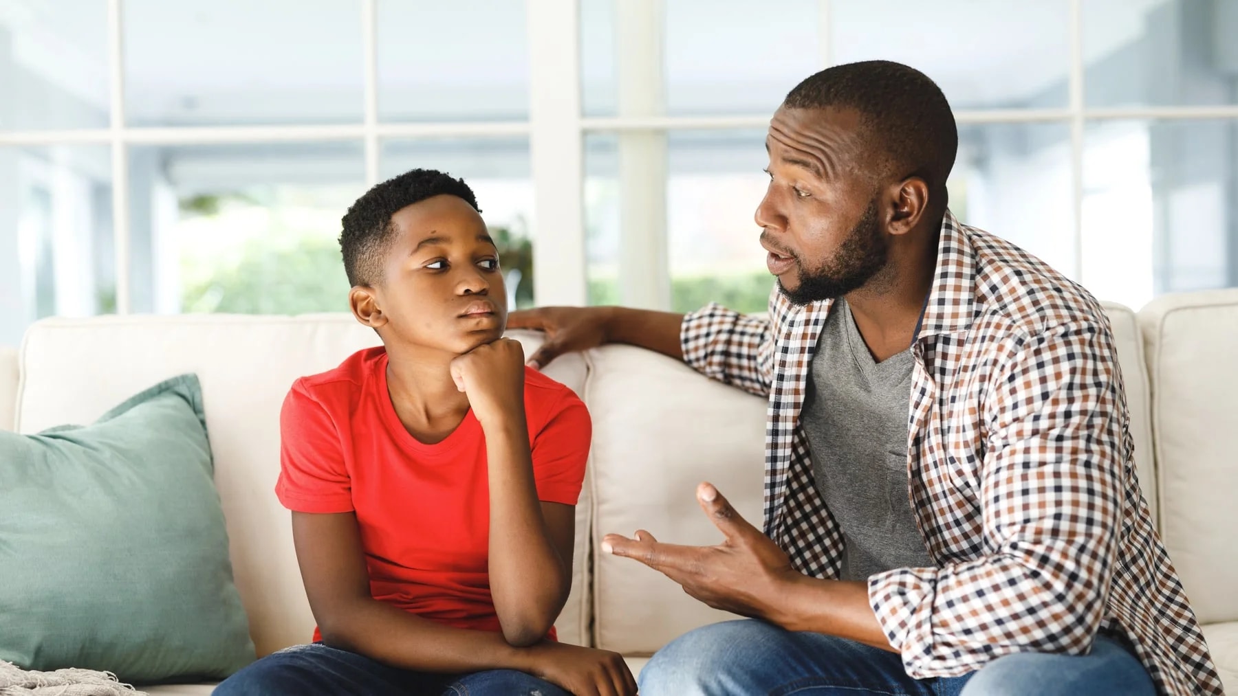 Pai e filho adolescente sentados no sofá durante uma conversa séria